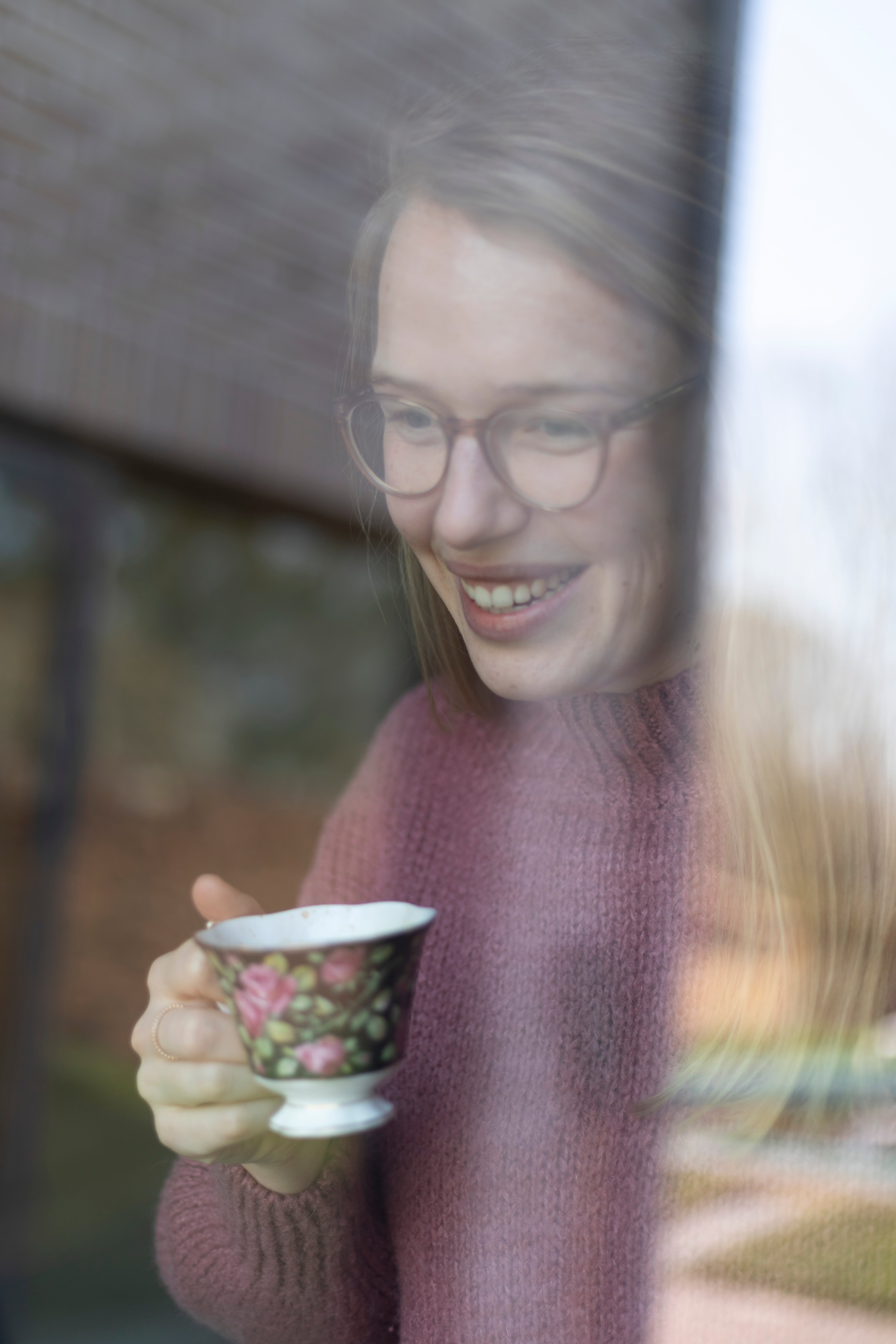 Indra achter een raam met een kopje koffie